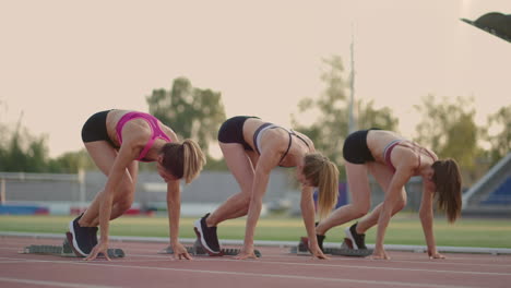 Three-young-women-in-the-stadium-on-the-start-line-in-blocks-start-in-the-race-in-slow-motion